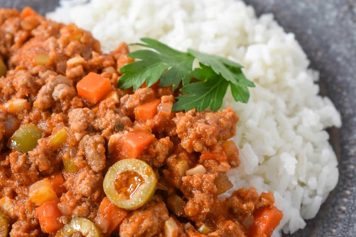 A close up image of the picadillo, served with white rice and garnished with parsley.