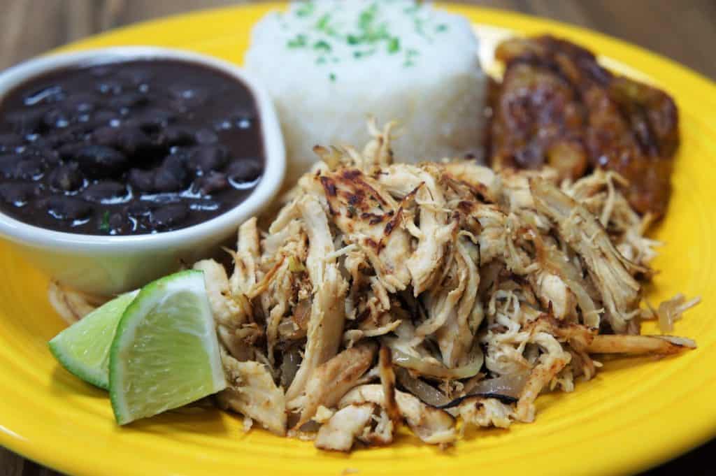 Vaca frita de pollo shredded crispy chicken with mojo marinade served on a yellow plate with white rice, black beans and fried sweet plantains on the side
