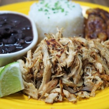 Vaca frita de pollo shredded crispy chicken with mojo marinade served on a yellow plate with white rice, black beans and fried sweet plantains on the side