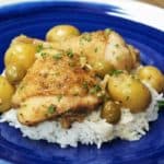 White chicken fricassee, stewed chicken with whole baby potatoes, green olives on a bed of white rice, served on a blue plate