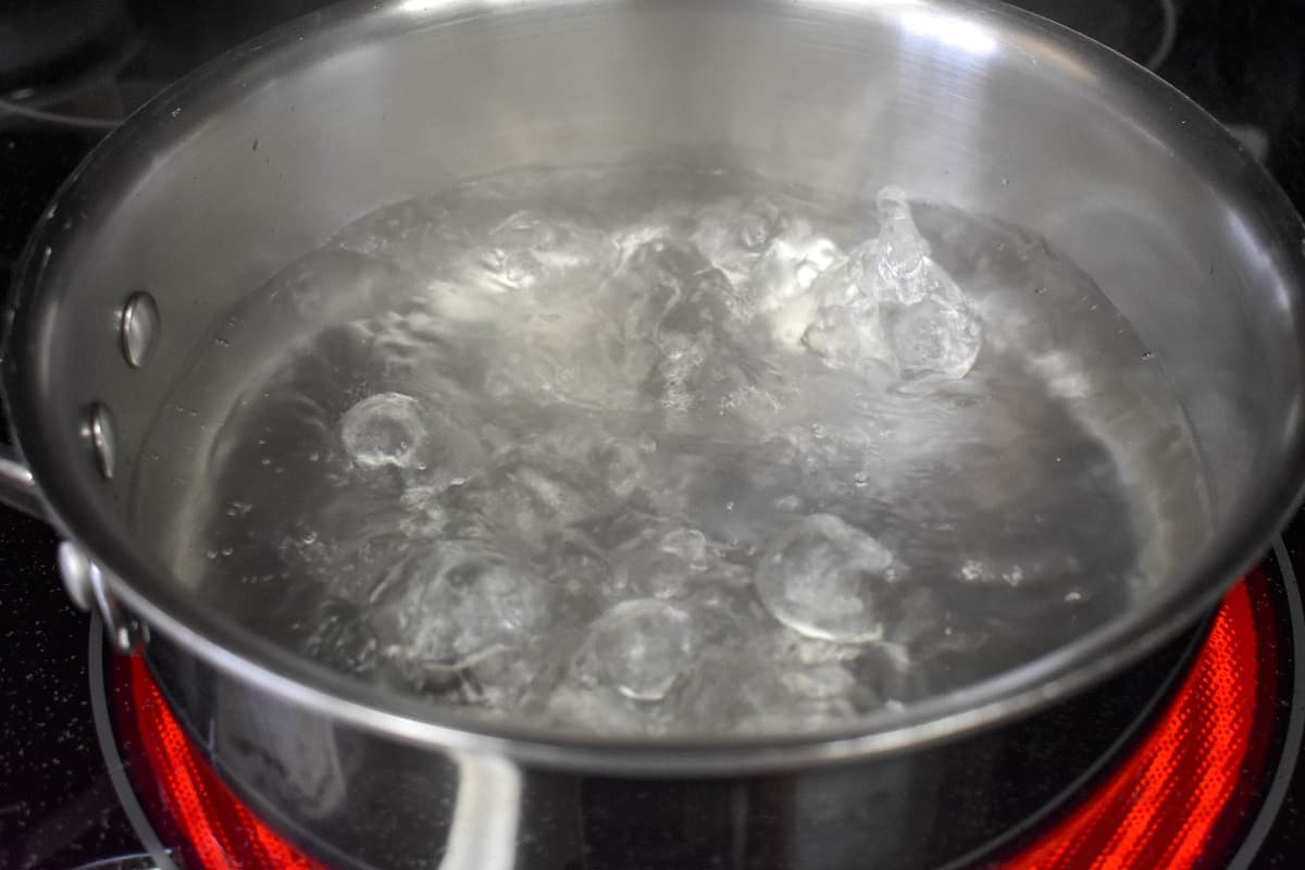 A saucepan with boiling water on an glass stovetop.