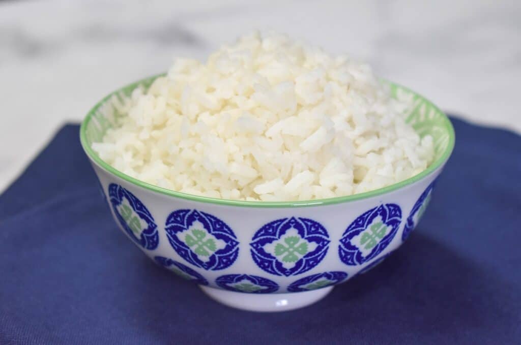 White rice mounded in a small, decorative blue and white bowl, displayed on a blue linen.