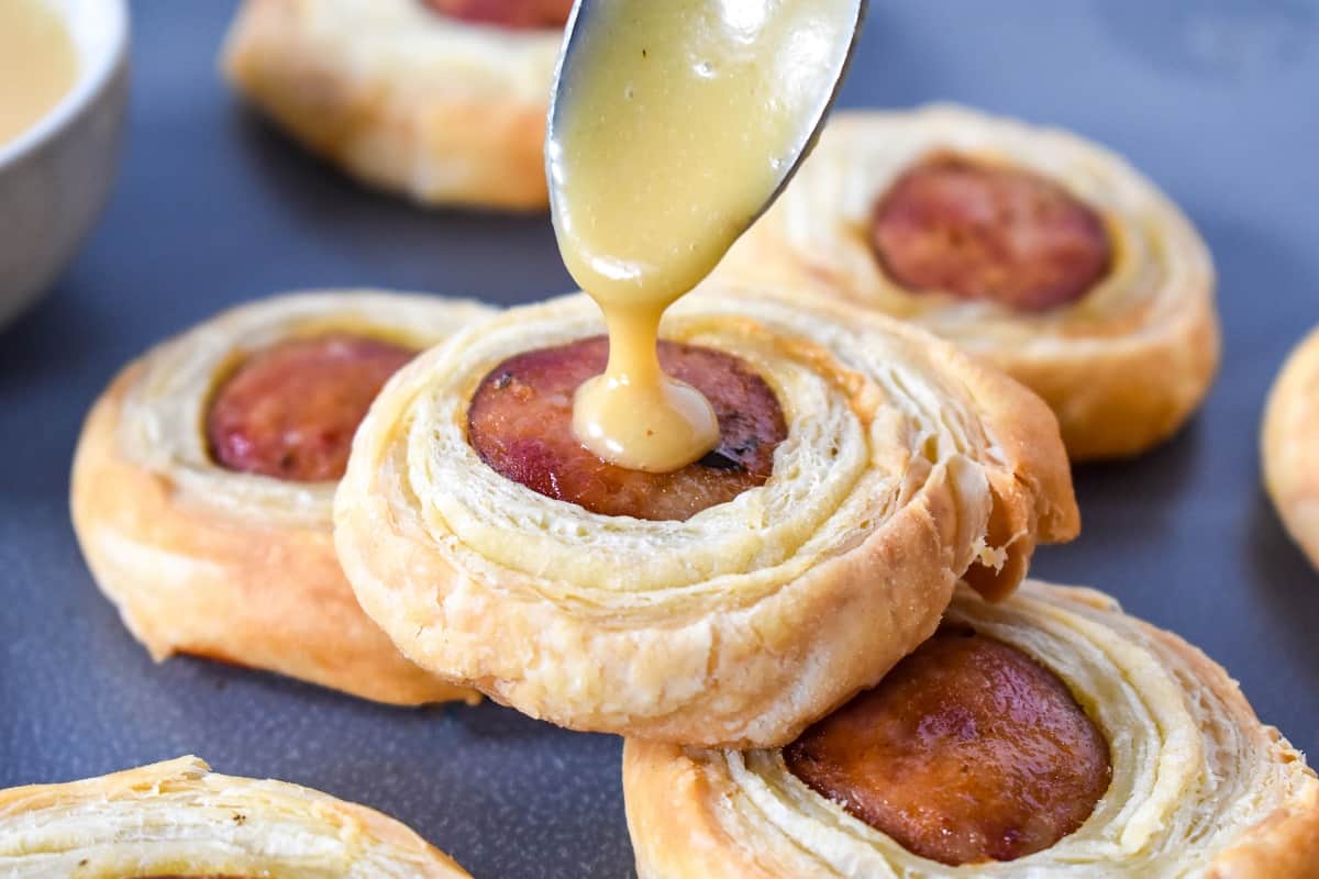 A close up of the sausage pastry with a spoon adding a drop of the mustard honey sauce.
