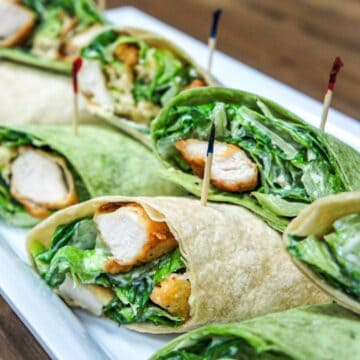 The chicken Caesar salad wraps cut in half, secured with a frilly toothpick and arranged on a white platter.