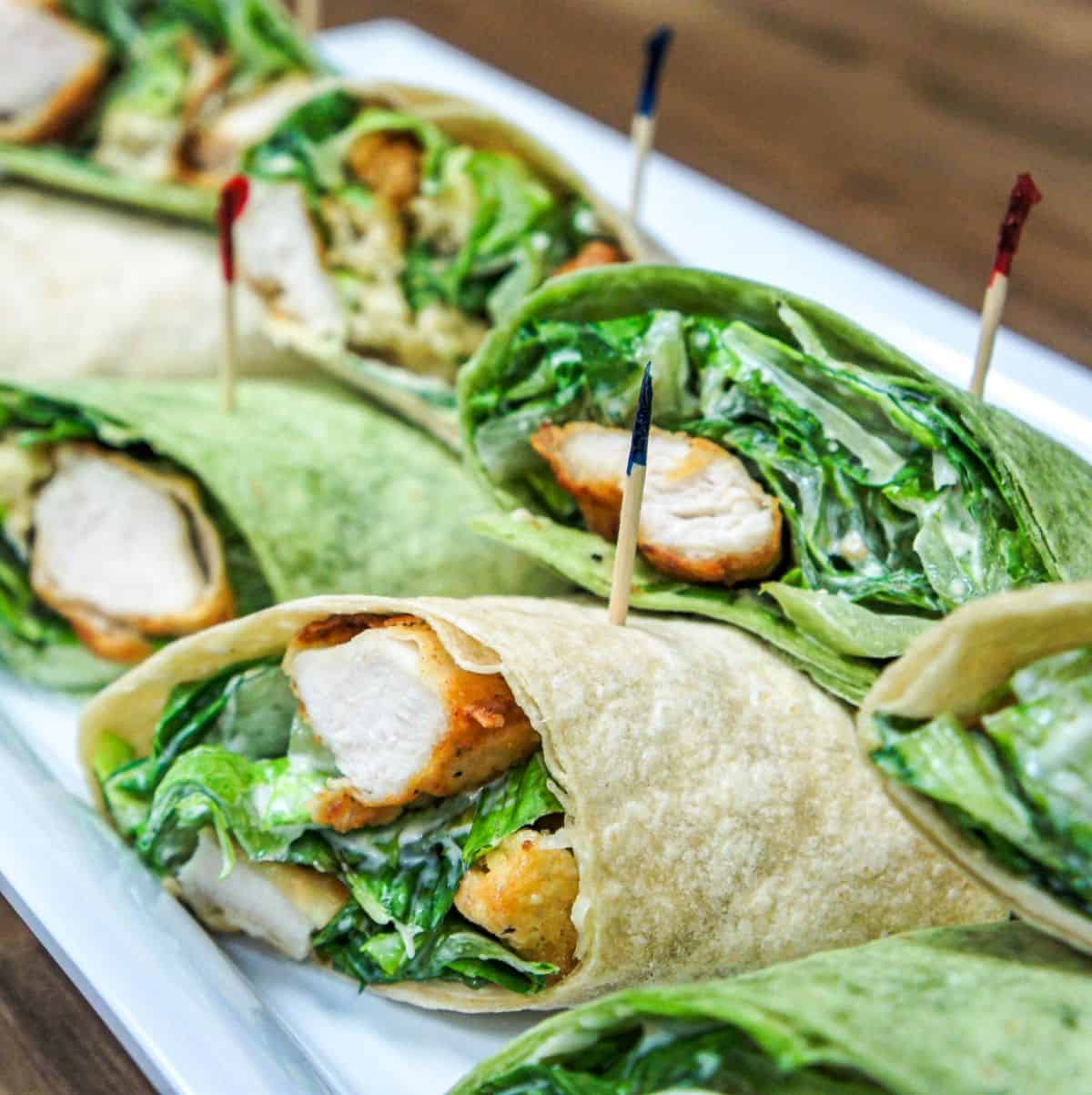 The chicken Caesar salad wraps cut in half, secured with a frilly toothpick and arranged on a white platter.