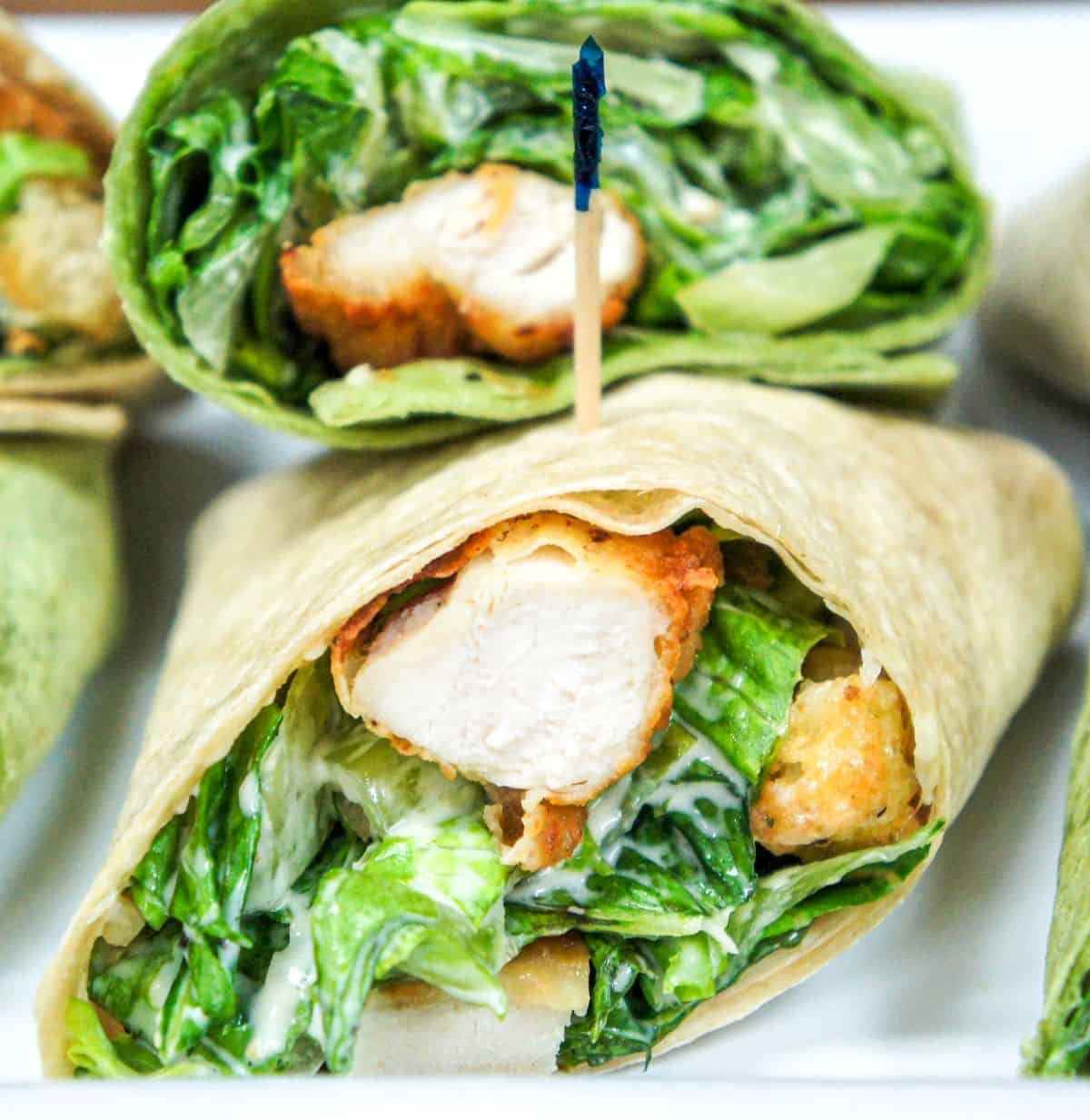 The chicken Caesar salad wraps cut in half, secured with a frilly toothpick and arranged on a white platter.