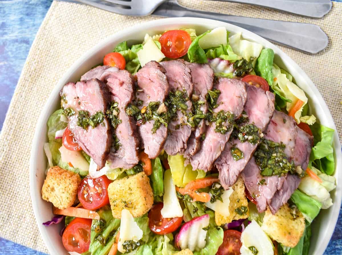 A close up of the finished dish with the chimichurri dressing on the sliced steak pieces.