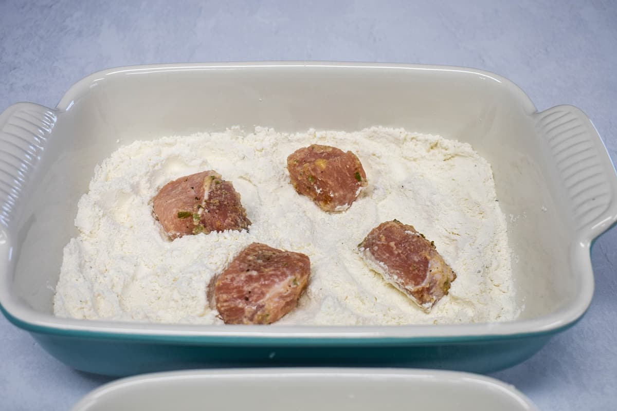 Four pork chunks set in flour in a baking dish.