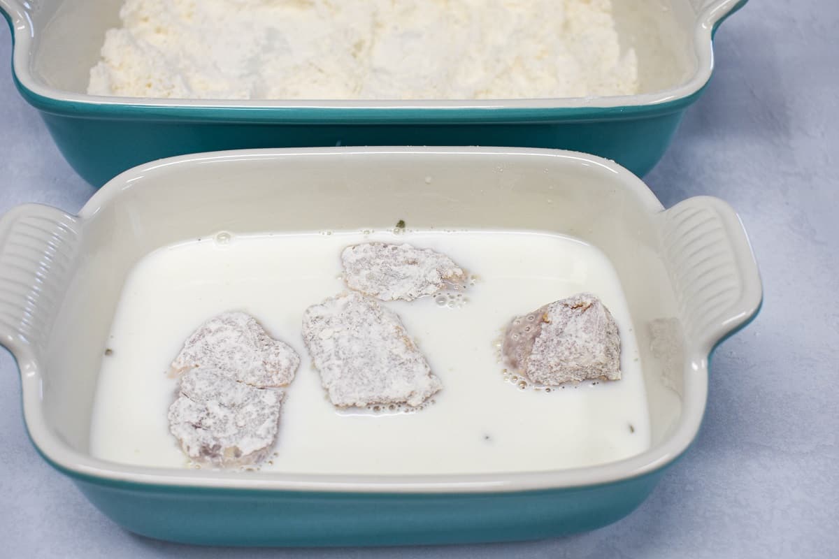 Four pork pieces that are lightly coated in flour placed in a pan with milk.