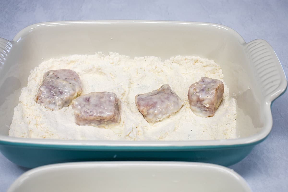 The pork pieces coated with one layer of flour and dipped in milk, placed back in the pan with flour.
