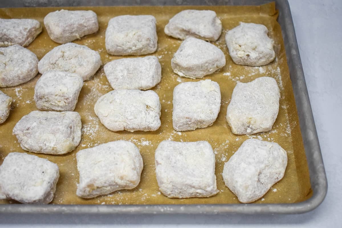 Pork pieces coated in flour and arranged on a baking sheet lined with parchment paper.