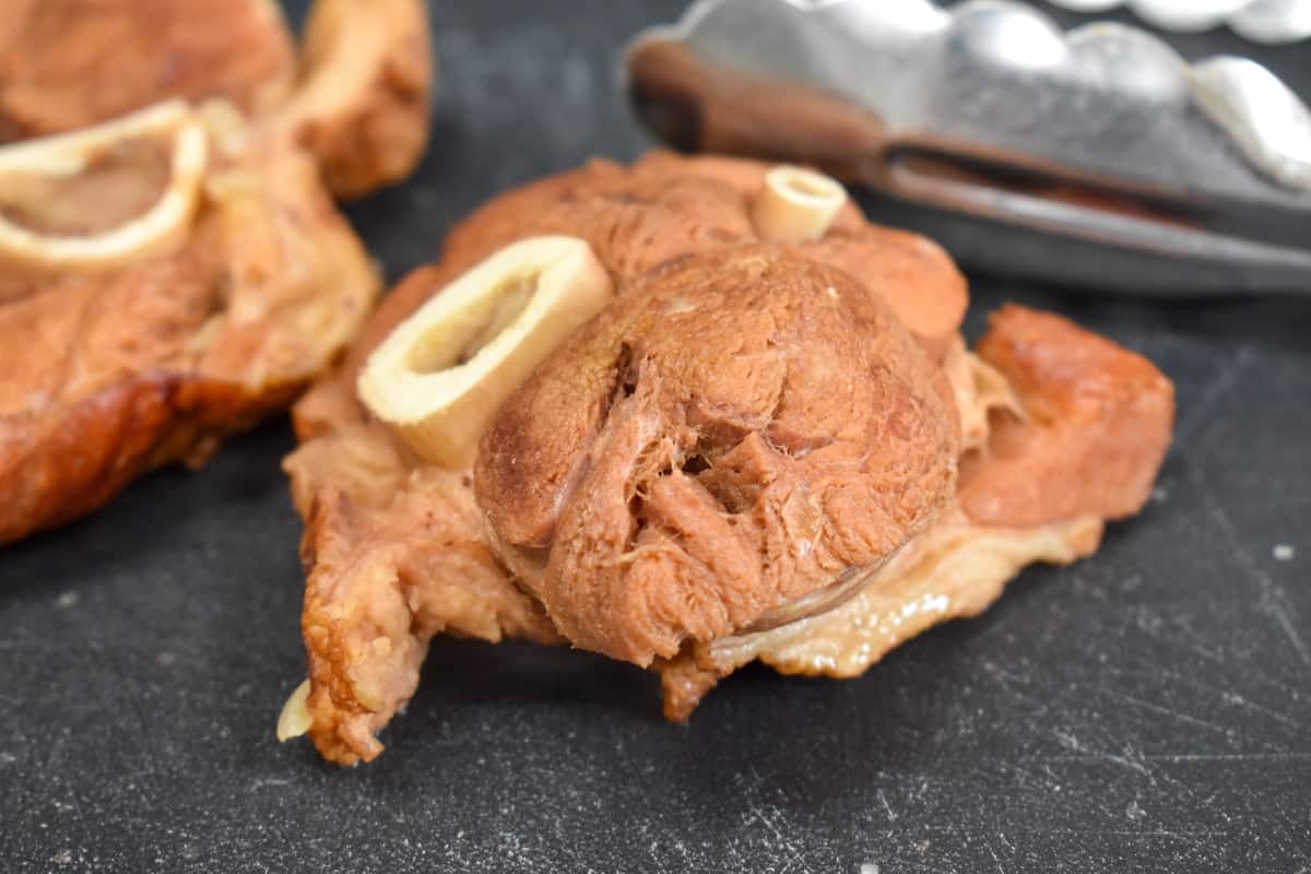 Cooked, sliced ham shanks on a black cutting board.