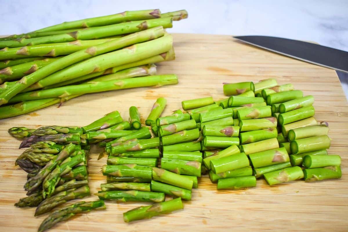 Fresh asparagus trimmed and cut into 1-inch pieces on a wood cutting board.