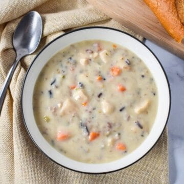 Overhead view of creamy chicken and wild rice soup with chicken, wild rice, carrots, and celery, served with crusty bread.