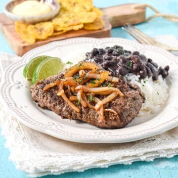 Cuban cube steak topped with sautéed onions served with white rice, black beans, and lime wedges.