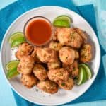 Fried pork chunks on a white plate with a small bowl of hot sauce and lime wedges. The plate is set on a teal linen.