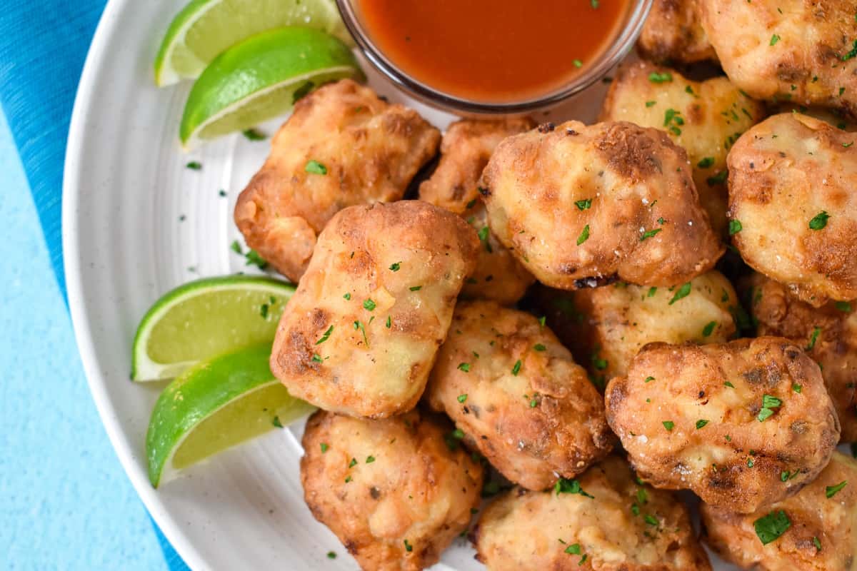 A close up of the fried pork set on a white plate served with hot sauce and lime wedges.