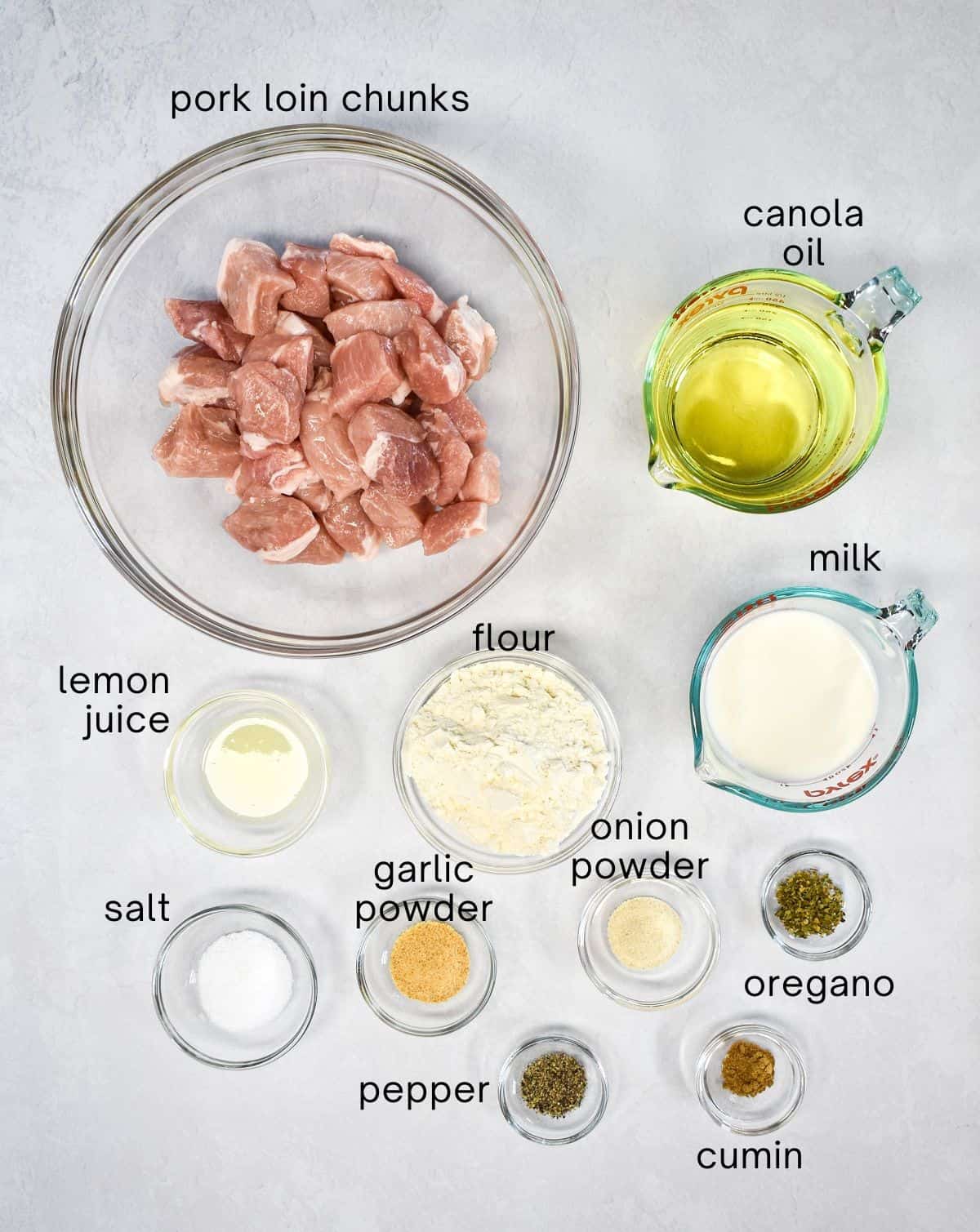 The ingredients for the pork chunks arranged in glass bowls on a white table. Each one is labeled with small, black letters.