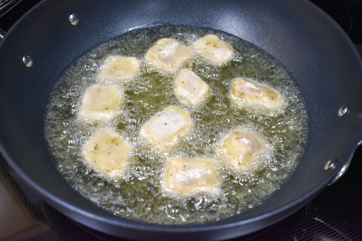 Flour coated pork chunks frying in a large, black skillet.