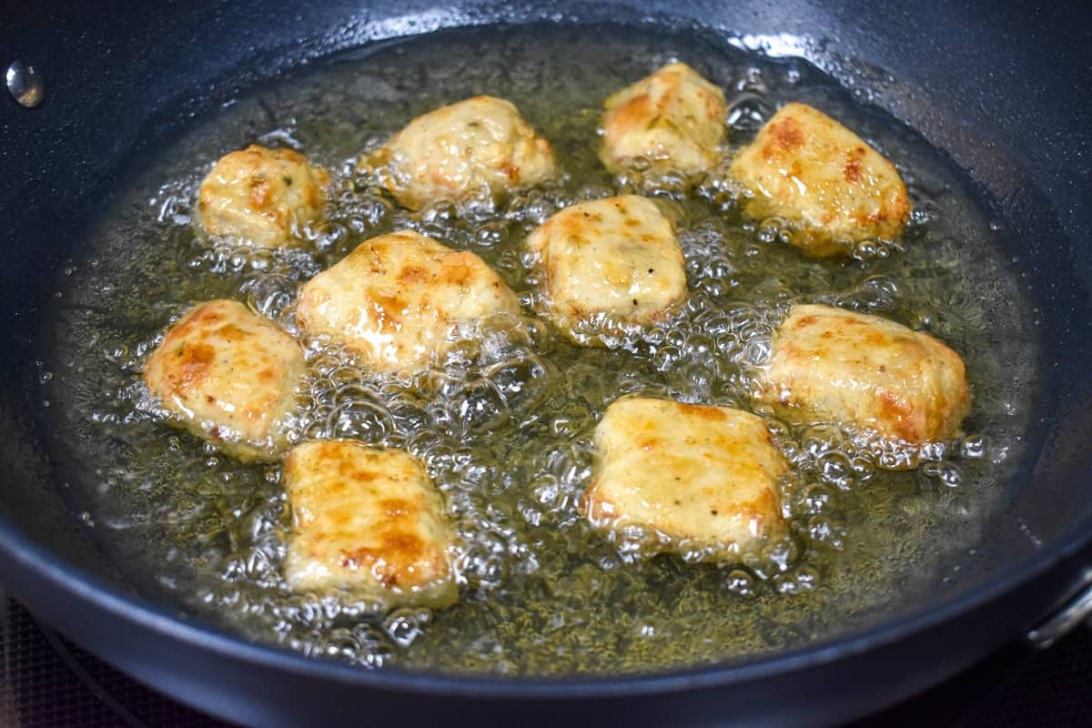 Lightly golden pieces of flour coated pork frying in a large, black skillet.