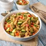 Garden pasta salad with tricolor rotini, tomatoes, and cucumber in a white serving bowl.