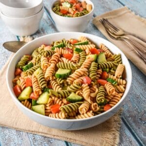 Garden pasta salad with tricolor rotini, tomatoes, and cucumber in a white serving bowl.