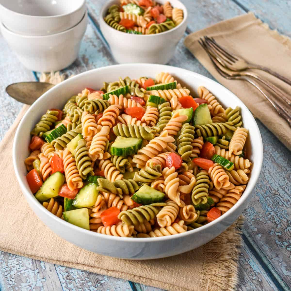 Garden pasta salad with tricolor rotini, tomatoes, and cucumber in a white serving bowl.