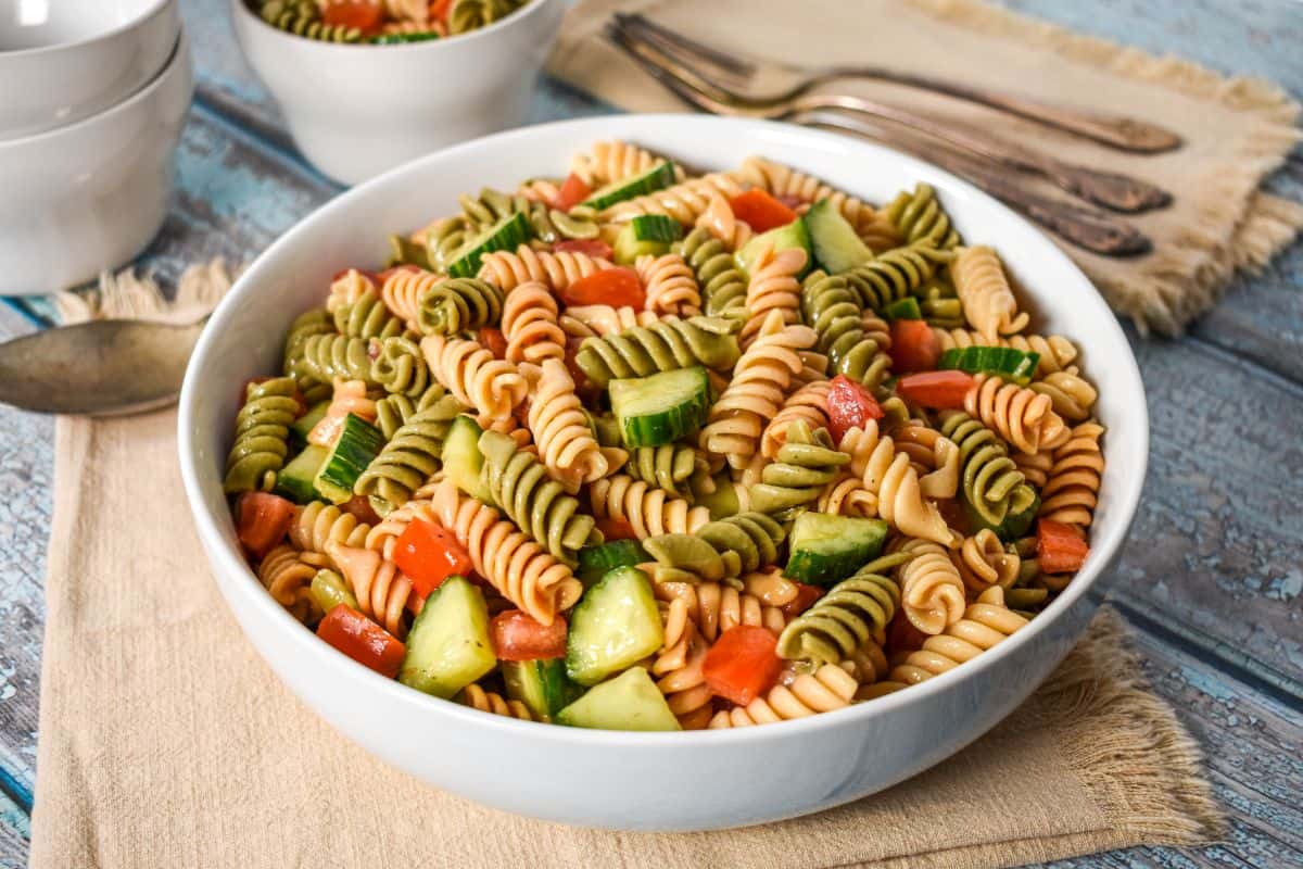 Garden pasta salad with tricolor rotini, tomatoes, and cucumber in a white serving bowl.