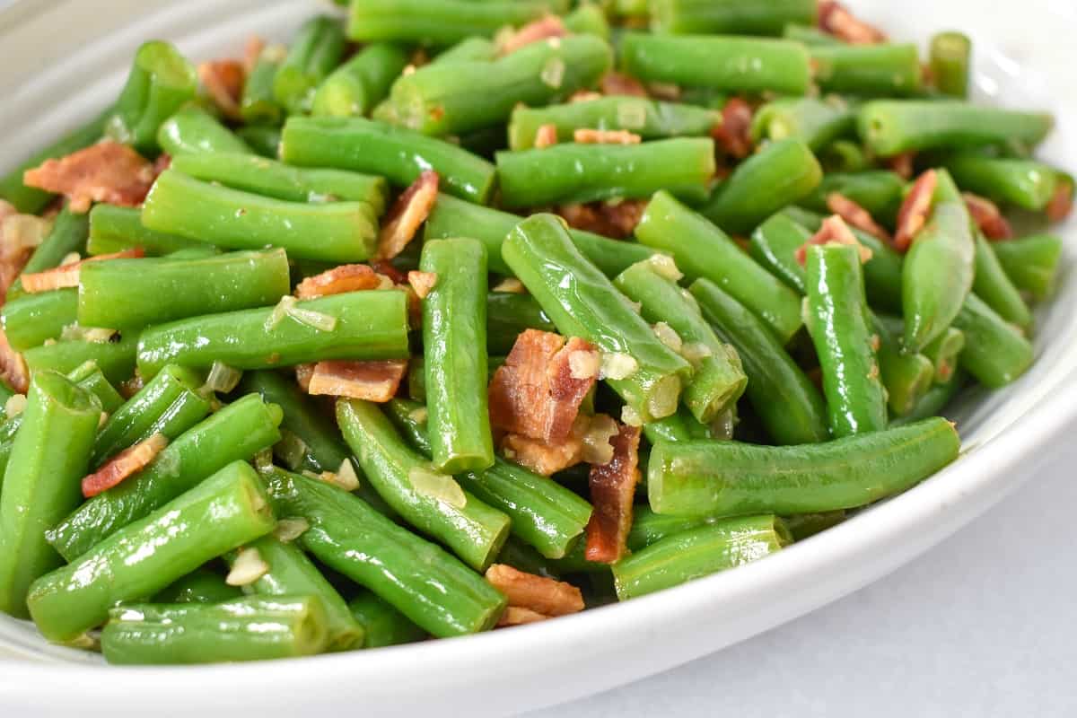 A close up of the bacon green beans served in a white bowl.