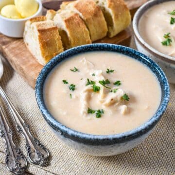 Bowl of homemade cream of chicken soup with pieces of chicken and chopped parsley, served with crusty bread and butter.