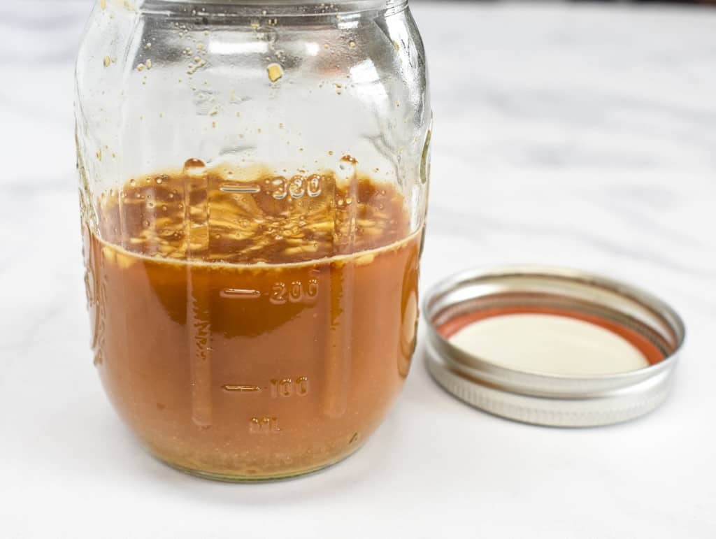 The prepared sauce in a canning jar with the lid to the right side and displayed on a white table.