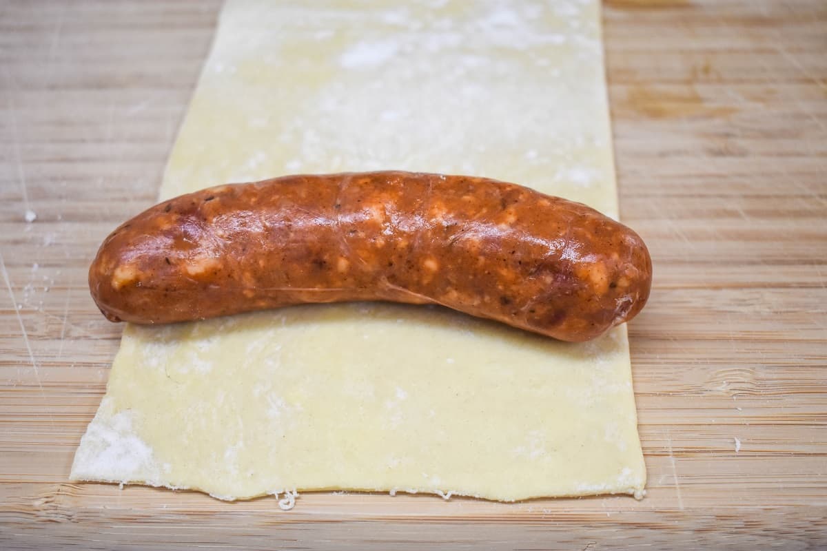 Andouille sausage placed on the edge of a puff pastry piece on a wood cutting board.