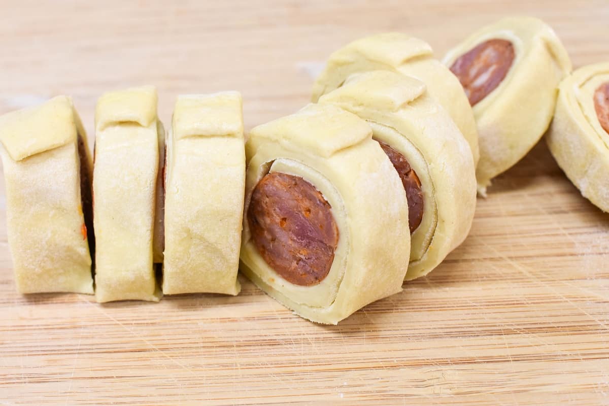 The puff pastry sausage roll cut into slices on a wood cutting board.