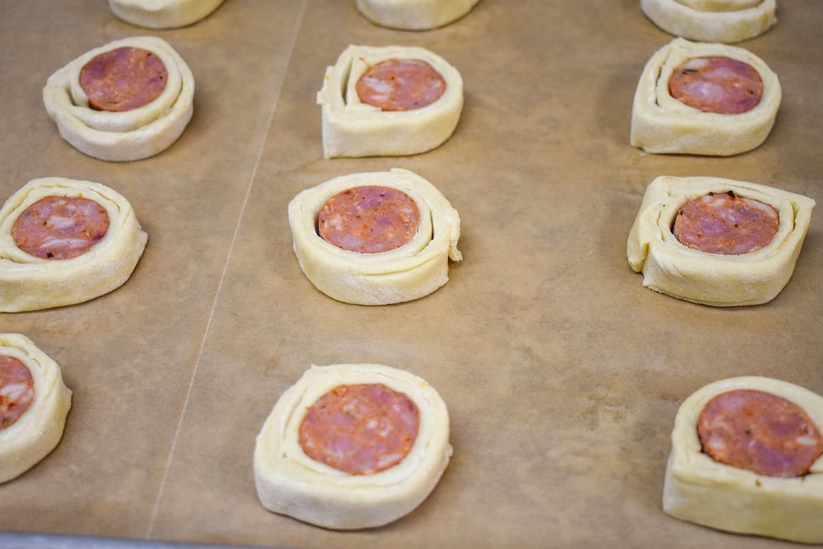 The sausage pastry slices placed on a baking sheet lined with brown parchment paper.