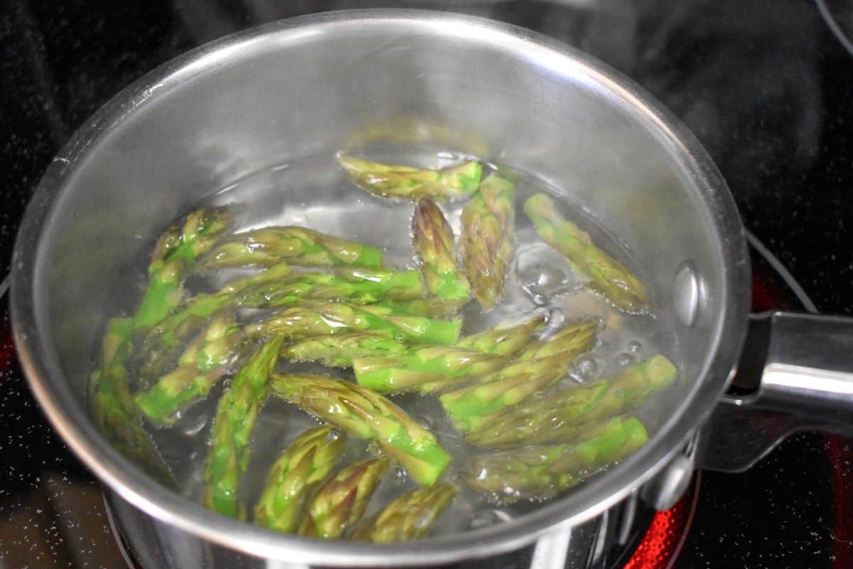 Reserved asparagus tips blanching in boiling water in a small saucepan.