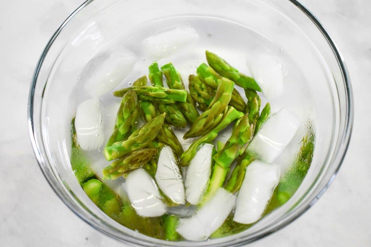 Blanched asparagus tips cooling in a bowl of ice water.