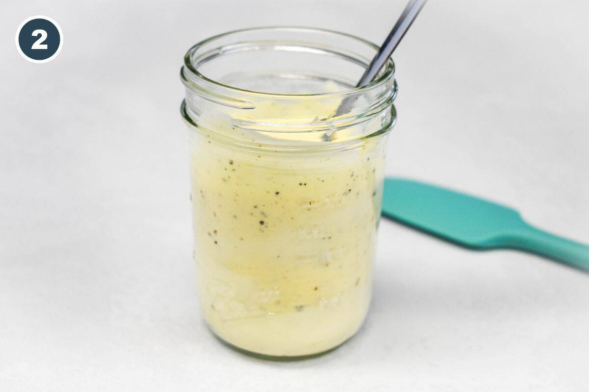 Creamy chicken salad dressing stirred together in a glass jar.