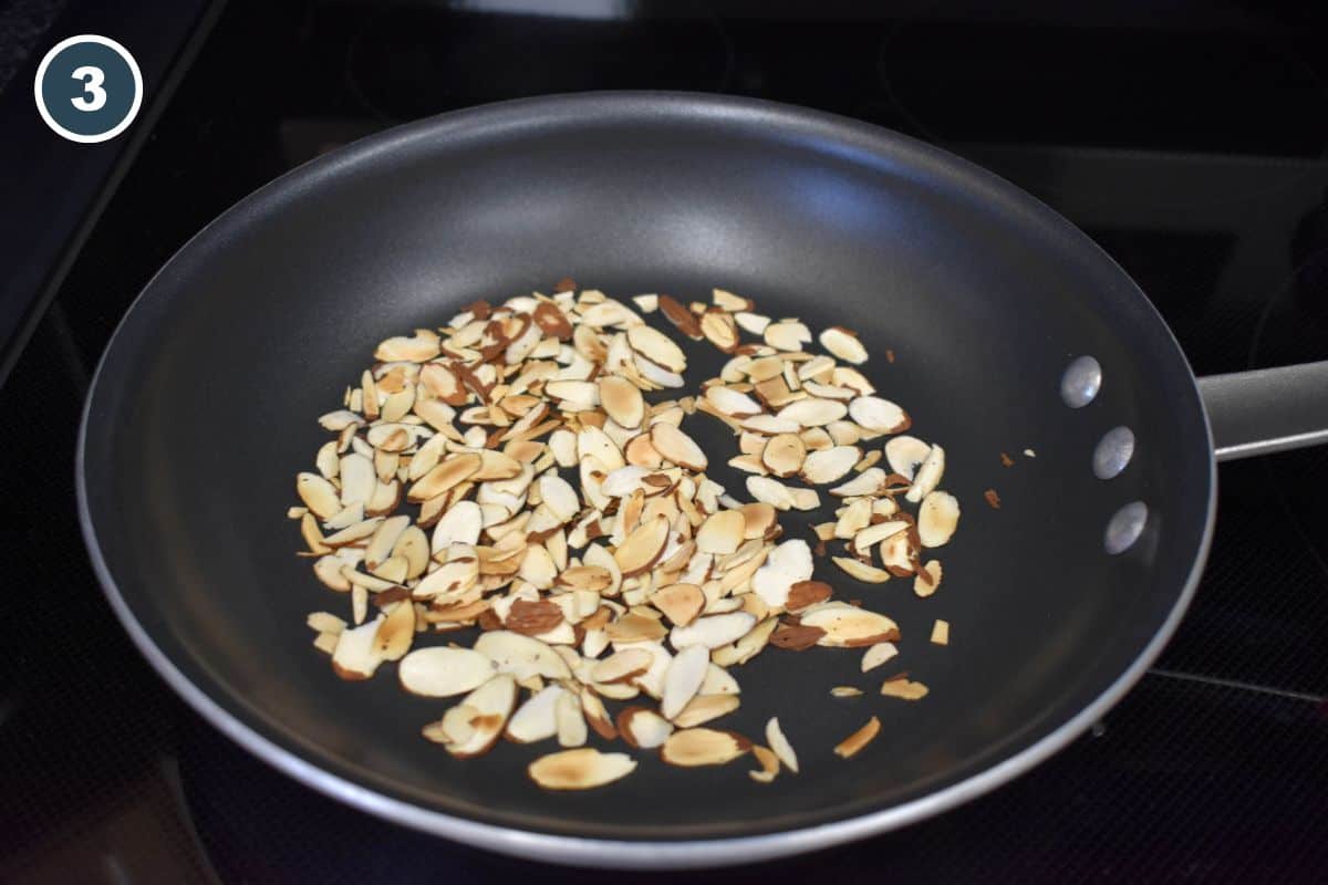 Sliced almonds toasting in a dry skillet until lightly golden.