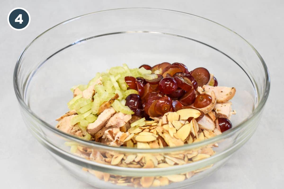 Cooked chicken, celery, red grapes, and toasted sliced almonds in a large mixing bowl.