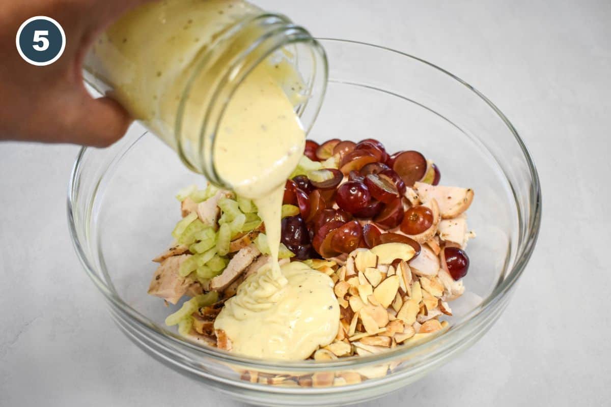 Creamy dressing being poured over the chicken, celery, grapes, and toasted almonds.