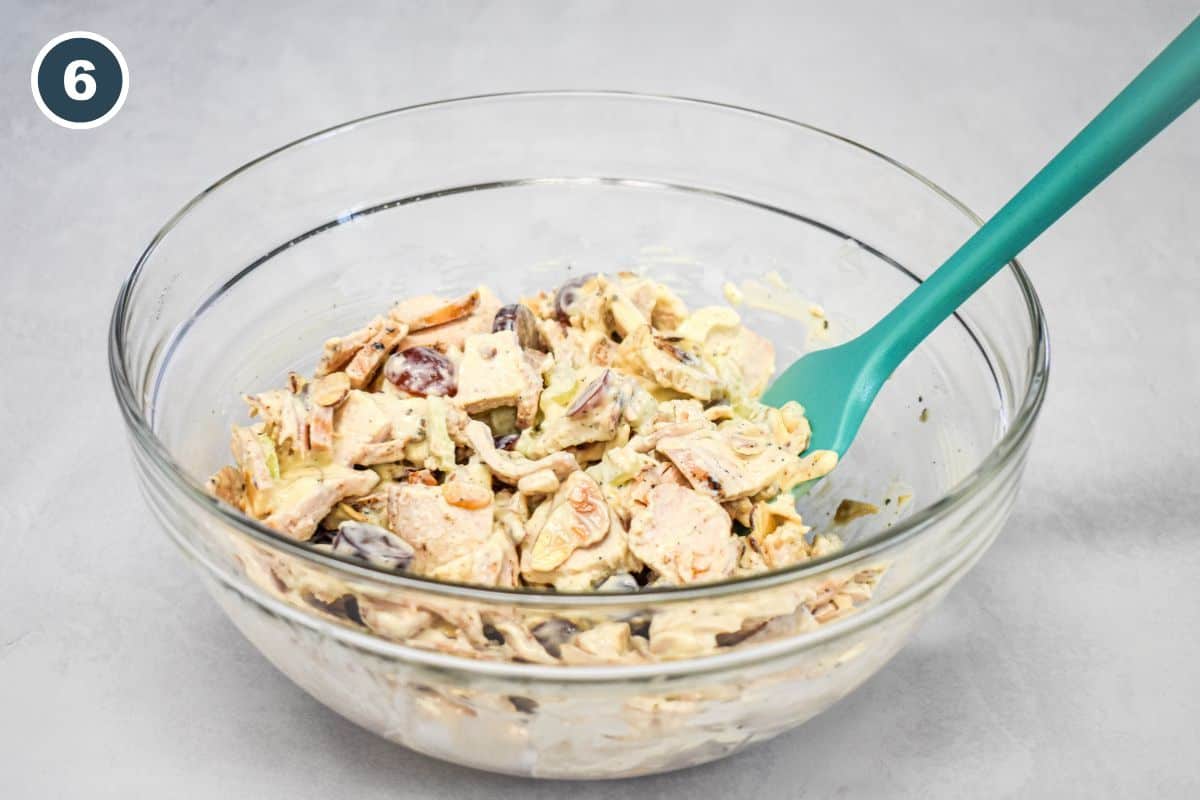 Chicken salad mixed with grapes, celery, and toasted almonds in a large glass bowl.