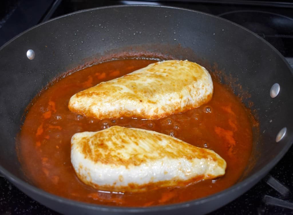 Two chicken breast added to the red sauce in a large, black skillet.