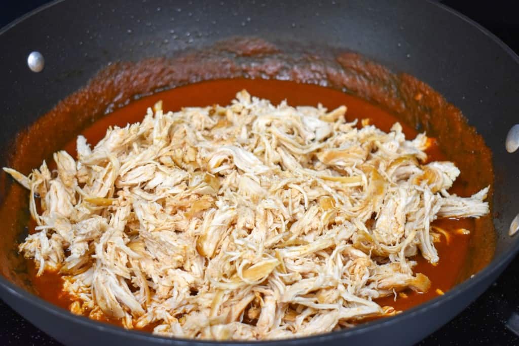 The shredded chicken breast added to the red sauce before being stirred.