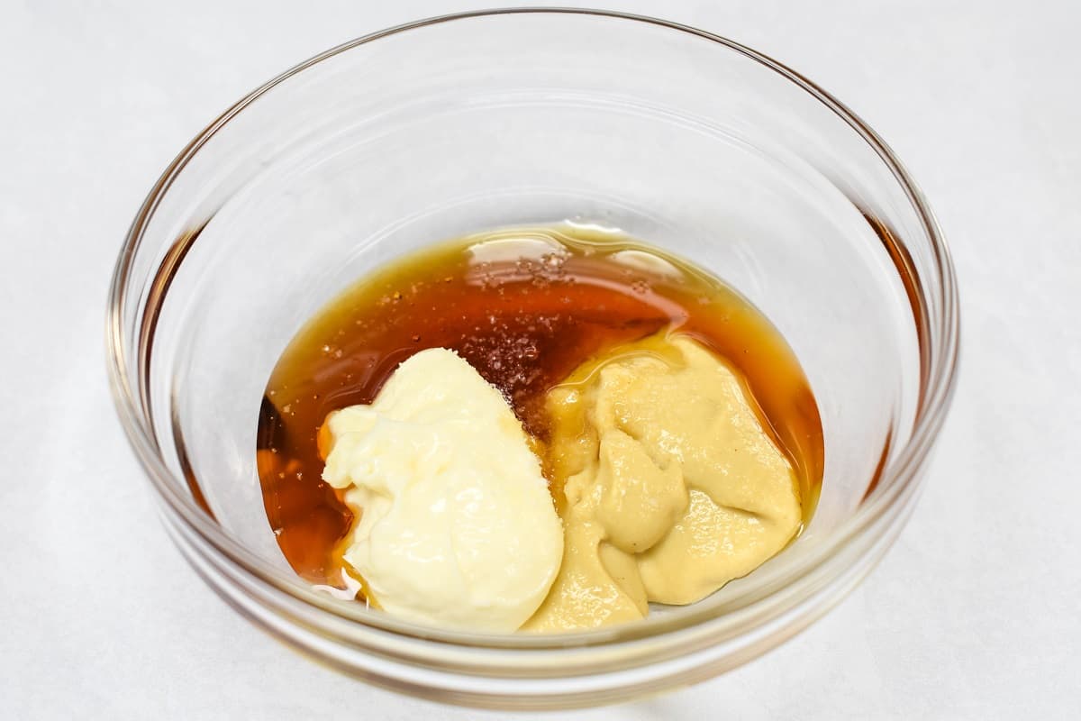 A small glass bowl with dijon mustard, mayonnaise, honey, and a pinch of salt.