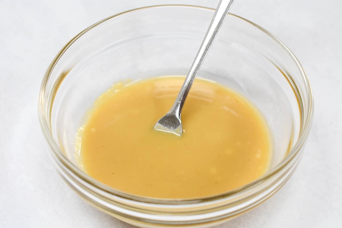 The finished dijon honey sauce in a small, glass bowl set on a white table.