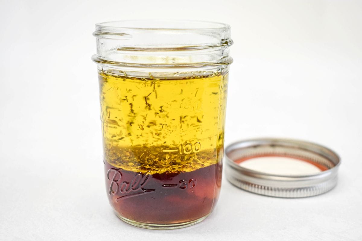 Olive oil, red wine vinegar, garlic, and seasonings layered in a glass jar.