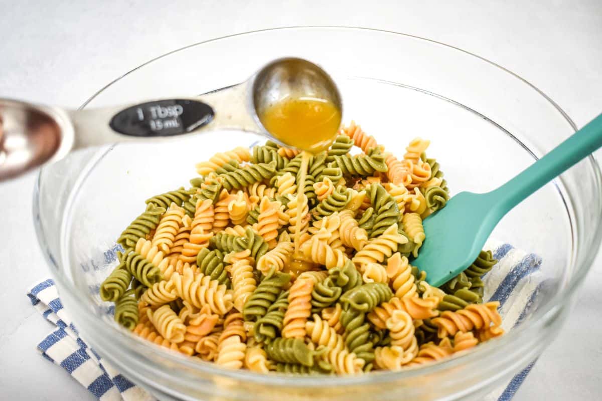 Dressing being added by the tablespoon to hot tricolor rotini.