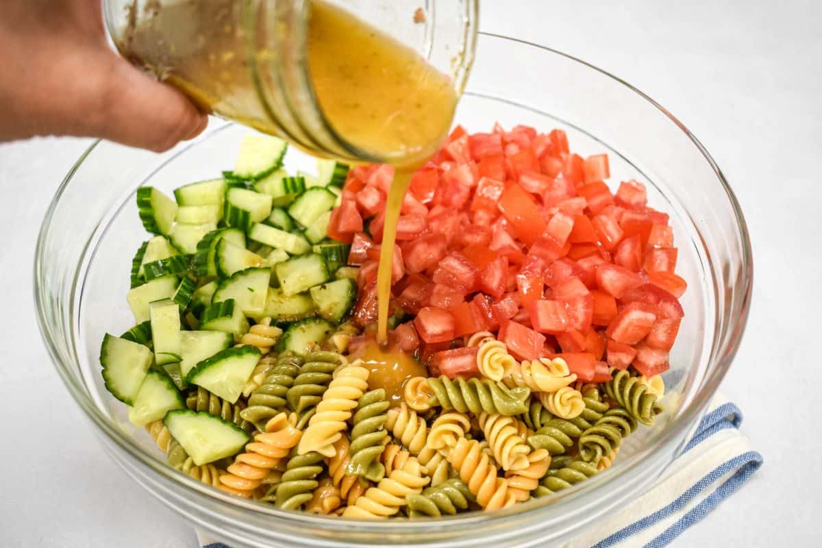 Remaining dressing being poured over rotini, tomatoes, and cucumber.