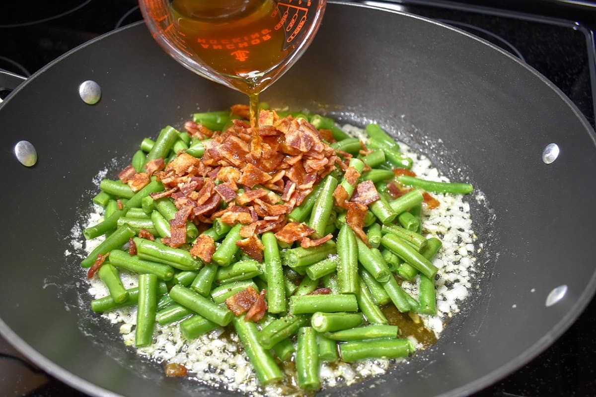 Beef broth being added to the ingredients in the skillet.