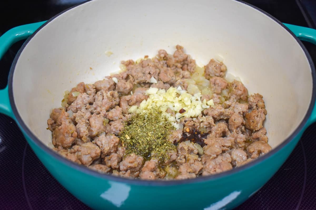 Browned sausage with diced onions, garlic, and seasoning cooking in a large pot.
